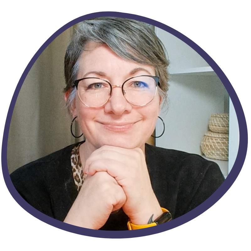 Mimi Scheibe - Portrait von Mimi, die lächelnd in die Kamera schaut, das Kind auf die Hände gestützt. Sie trägt einen schwarzen Pullover und eine Brille sowie eine Kurzhaarfrisur.